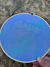 Load image into Gallery viewer, 8 Inch Silver &quot;Atlannuh&quot; Hand-Embroidered on Blue Oil Slick Iridescent Fabric Hoop
